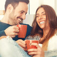 Couple sitting drinking from mugs and laughing Photo Thinkstock